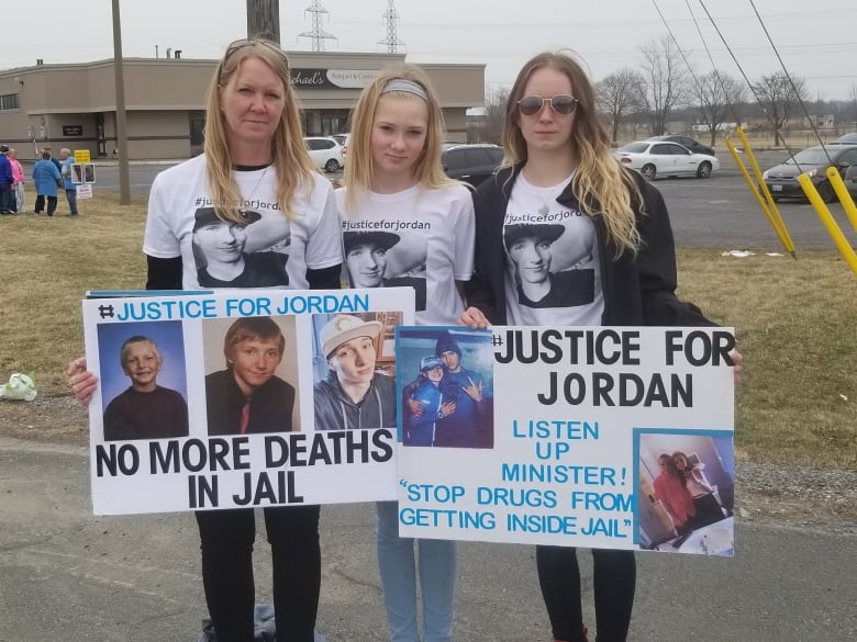 Three women stand with signs. 