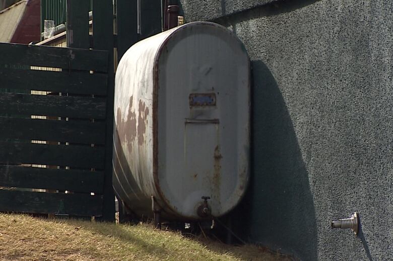 A home heating oil tank sits against a wall outside a residence.