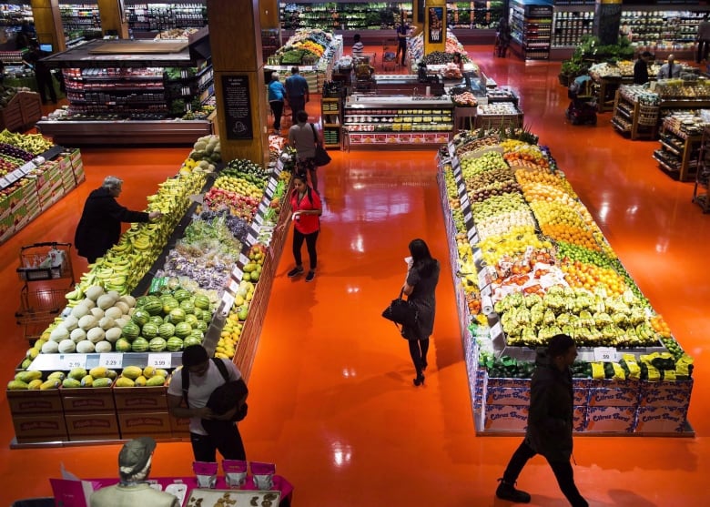 People walk around a produce section in a grocery store.