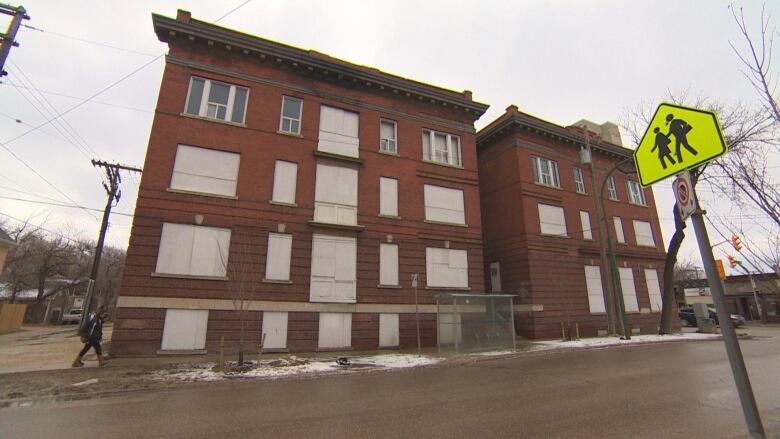 A three-storey brick building with boarded-up windows sits at the corner of an intersection, shot from across the street.