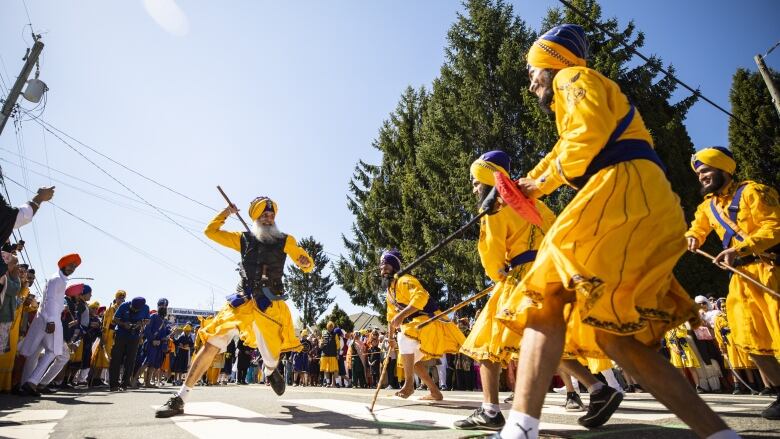 People in brightly-coloured attire sing and dance on city streets.