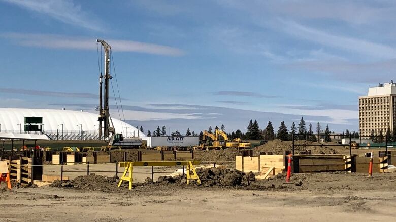 A crane towers over an halted construction site showing piles of dirt and machinery. There are no workers.