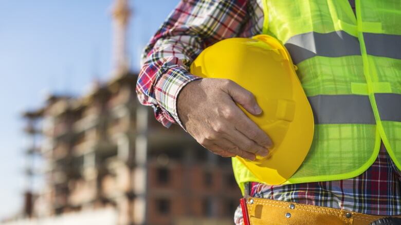 A close up of a man in a construction vest holding a safety helmet.