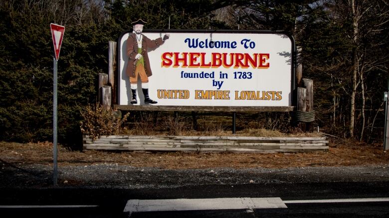 A sign is seen on the roadside saying 'Welcome to Shelburne, Founded in 1783 by United Empire Loyalists' with a cartoon of a Loyalist 