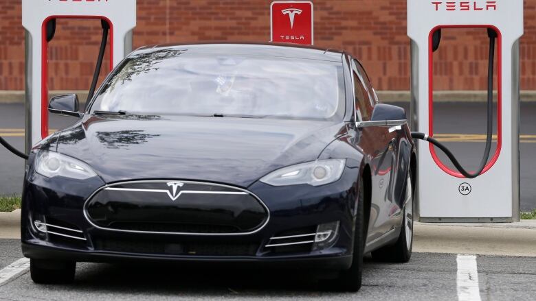 FILE- In this June 24, 2017, file photo, a Telsa Model 3 car recharges at a Tesla charging station at Cochran Commons shopping center in Charlotte, N.C. esla has cut $1,100 from the base price of its Model 3 car designed for the mass market.  The electric car company now says on its website that the car starts at $42,900, still short of the target base price of $35,000.  For $42,900 buyers will get a rear-wheel-drive Model 3 in black with Teslas lower-range battery that goes 264 miles per charge. (AP Photo/Chuck Burton)