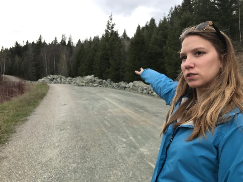 A woman in blue points at something far away on a road.