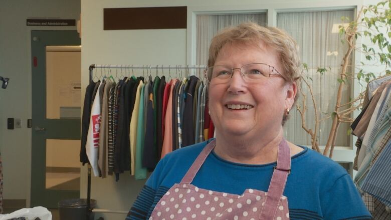 Smiling woman in front of clothing racks. 