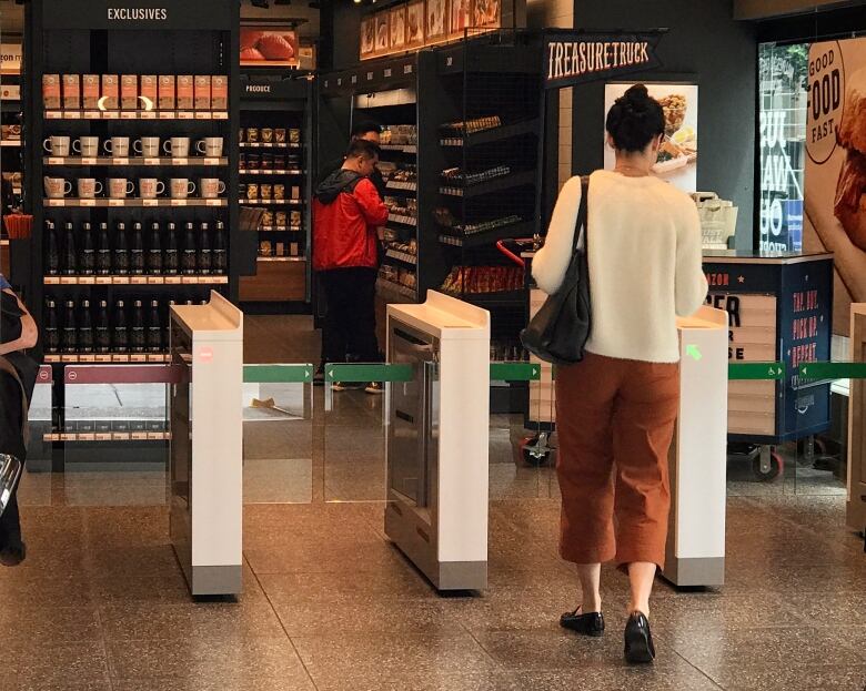 A woman is seen from behind as she walks through white and green gates into a grocery store