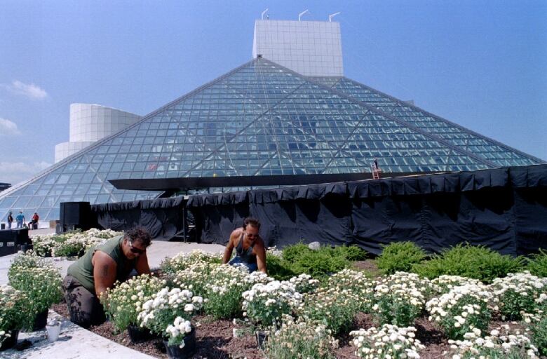 Two men plant flowers in front of a distinctive, pyramid shaped building.