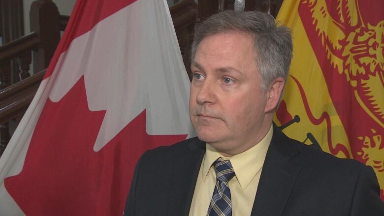 Glen Savoie stands in front of flags as he speaks to reporters