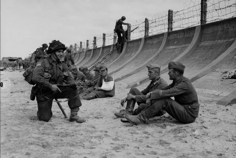 Two uniformed men sit on beach while another kneels nearby