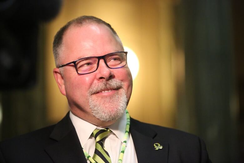 A man with glasses dressed in a suit is standing and smiling.