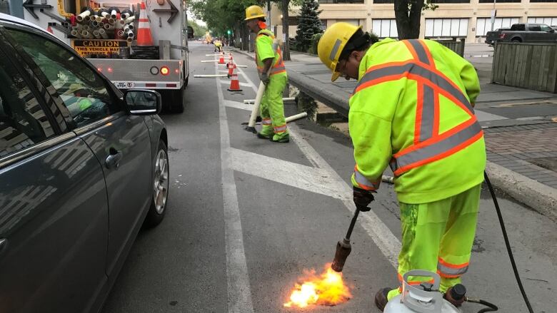 City worker has blow torch and is torching the road