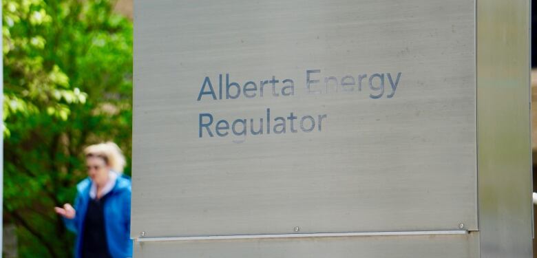 A sign for the Alberta Energy Regulator is visible outside a building. There is green foliage visible in the background.