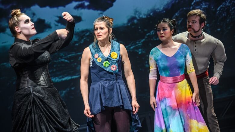 Four performers work on a stage. In the middle are two women in colourful clothing. On both sides are people in darker clothing.