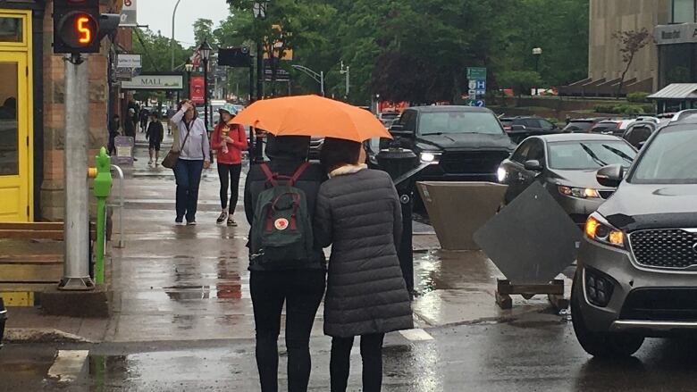 Pedestrians in downtown Charlottetown share an umbrella.