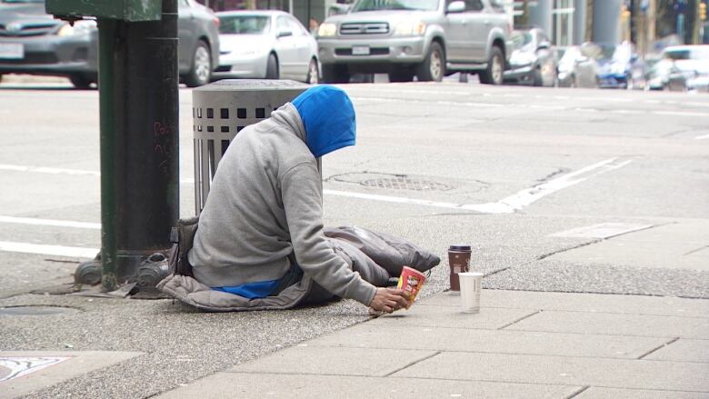 A man sits on the street with a cup.