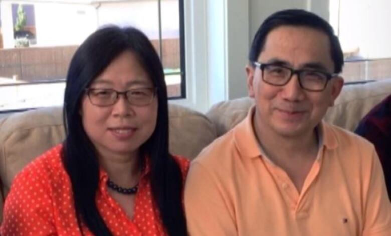 A man and woman sit side by side on a couch, smiling at the camera.