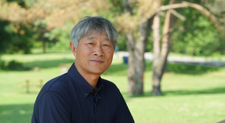 Man sits in front of green space. 