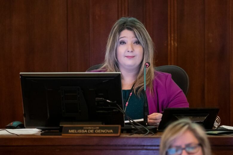 A white woman with blonde-streaked hair looks on as she sits in city council.