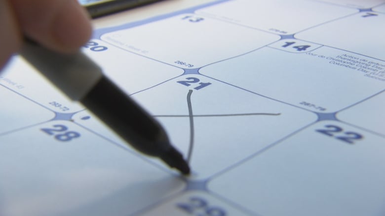 A pen, in a partially seen hand, crosses out the 21st day on a calendar. 