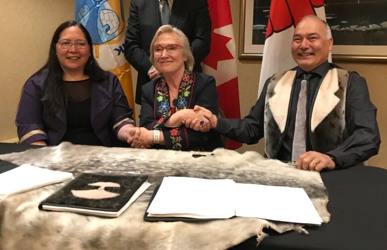 Three people shake hands, with two women on the left and one man on the right. 