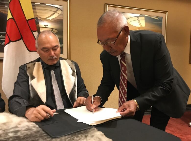 Two men signing a document at a desk.