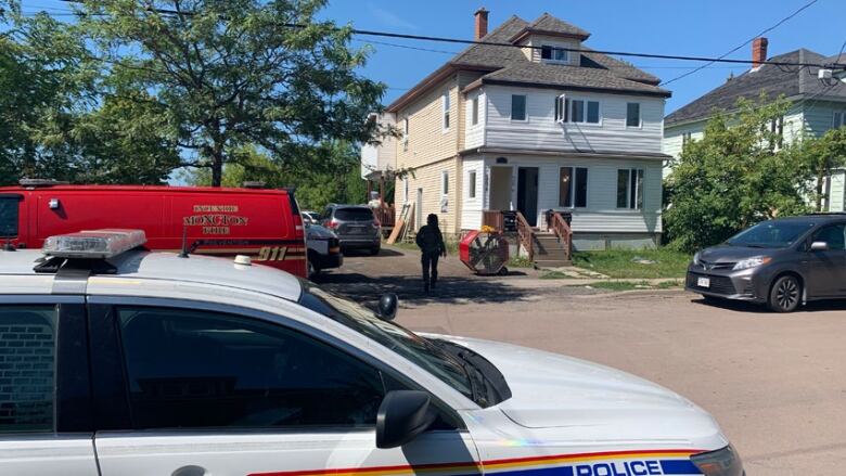 A two-storey house with police cars parked outside and a large fan in the driveway.