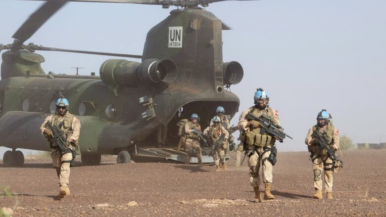 A large helicopter in a desert surrounded by soldiers.