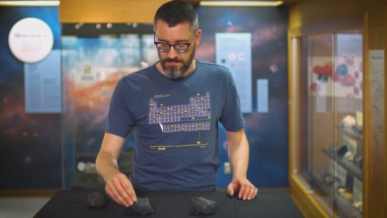 Man in periodic table t-shirt examines rocks on a table