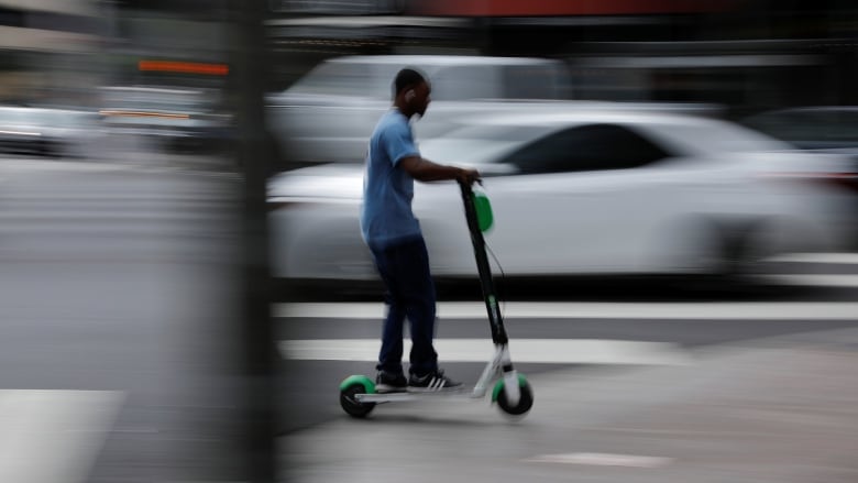 man speeds along a downtown street atop a Lime e-scooter in Los Angeles.