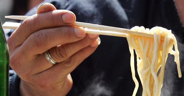 A man's hand is shown holding up chopsticks that hold noodles.