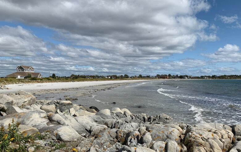 A beach with white sand stretches out from grey rocks, and a house is visible on the far left