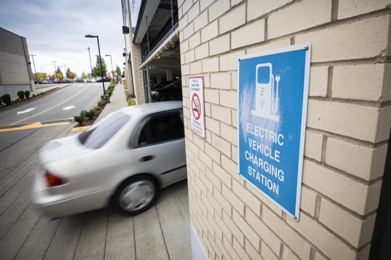 A car drives into a parking structure that displays a sign indicating it has an electric vehicle charging station. 