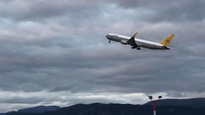 A passenger jet is seen taking off, with mountains in the background.