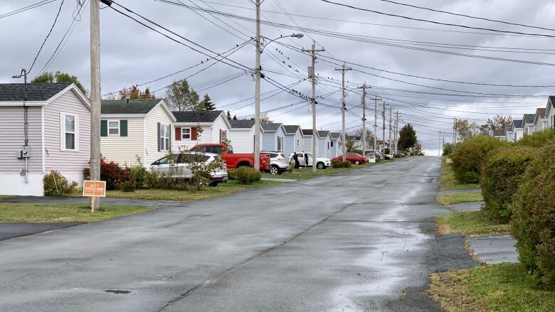 A line of about 10 homes on the side of a residential street that has bushes on the opposite side. 