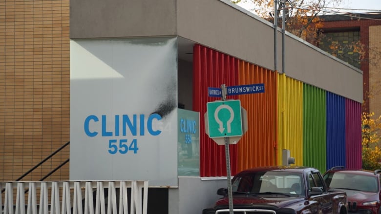 A brick one-storey building has a large rainbow sign painted on the side.