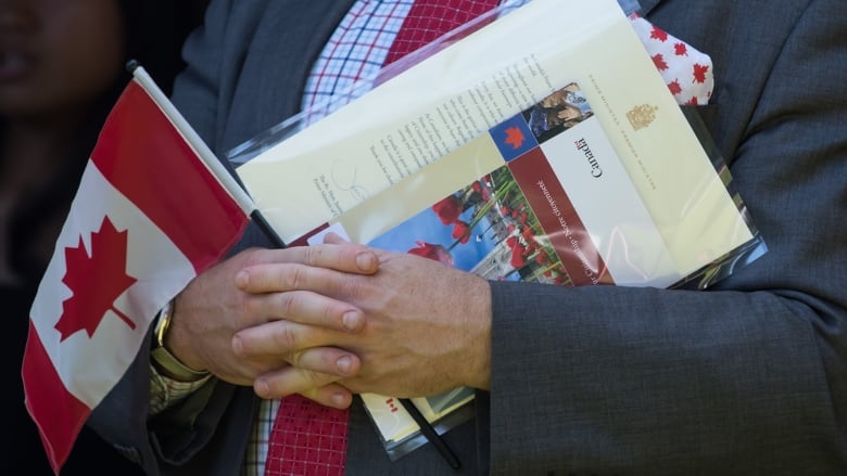 A new Canadian holds a flag, their citizenship certificate and a letter signed by Prime Minister Trudeau. 