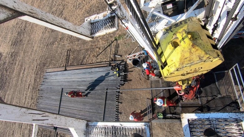 A top down view of workers in red suits and white helmets doing work on a large piece of yellow metal industrial equipment.