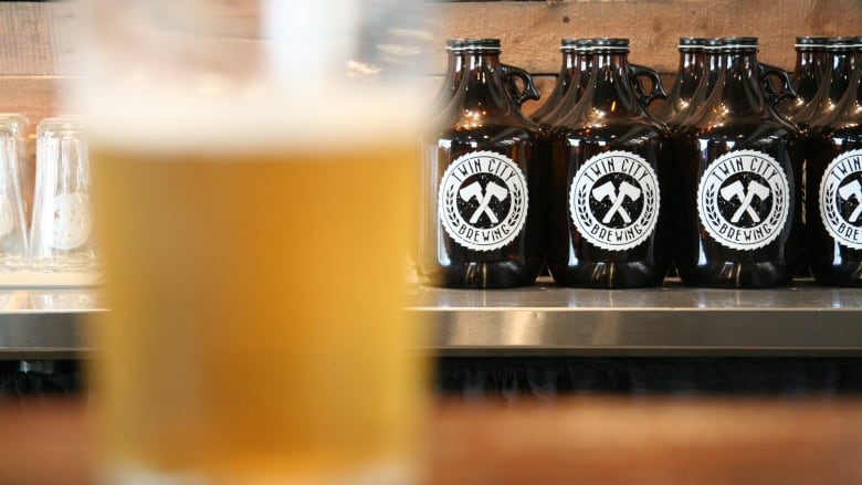 A row of glass growlers in the background with an out-of-focus glass of beer close up at the left of the picture.