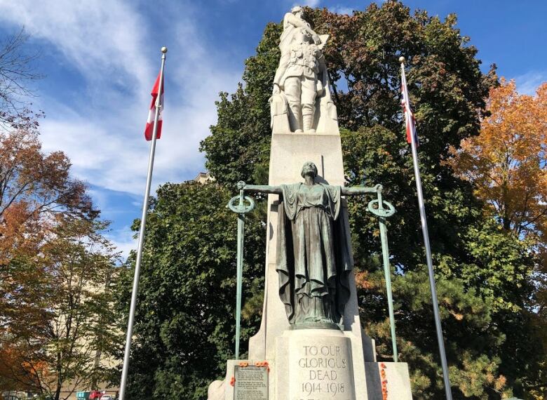 A stone monument shows a female figure in front with her arms out holding two swords. On top, a female figure holds a tablet and a soldier is looking at the tablet.