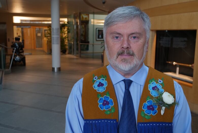 Man in dress shirt and moose hide vest looks at camera.