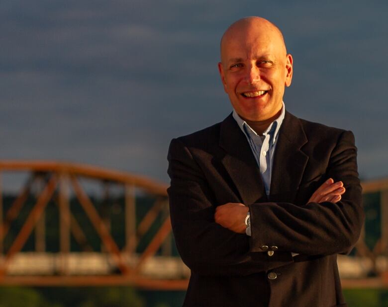 A bald man in a suit with a bridge in the background