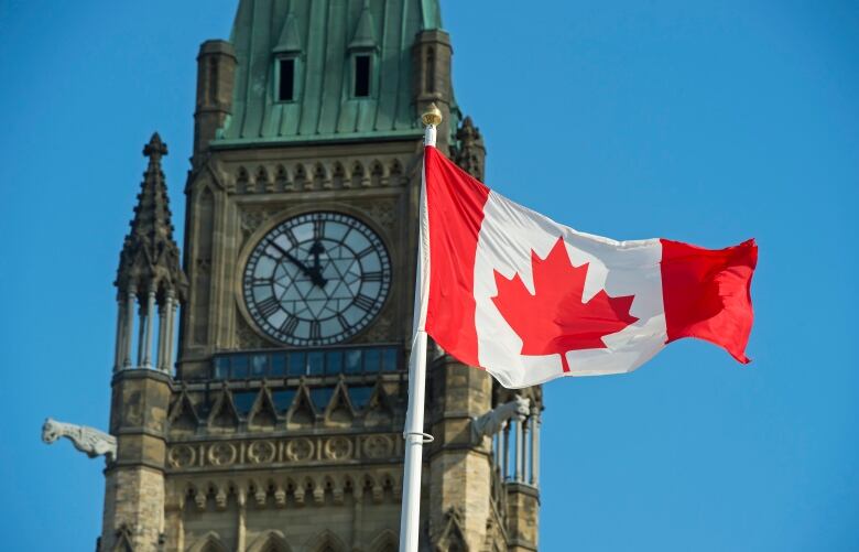 A clock tower with a Canadian flag waving.