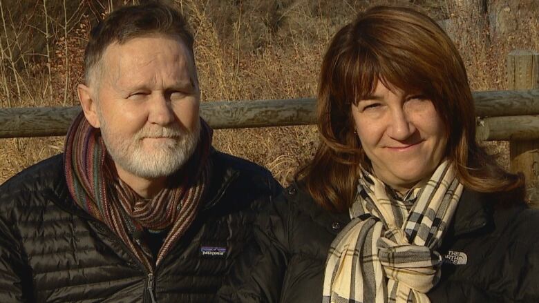 Jim Button, a middle-aged man with a grey beard, is outside beside his wife, Tracey, who has long brown hair. Both are wearing scarfs.