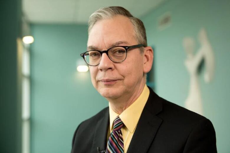 A man in horn-rimmed glasses stares into the camera.