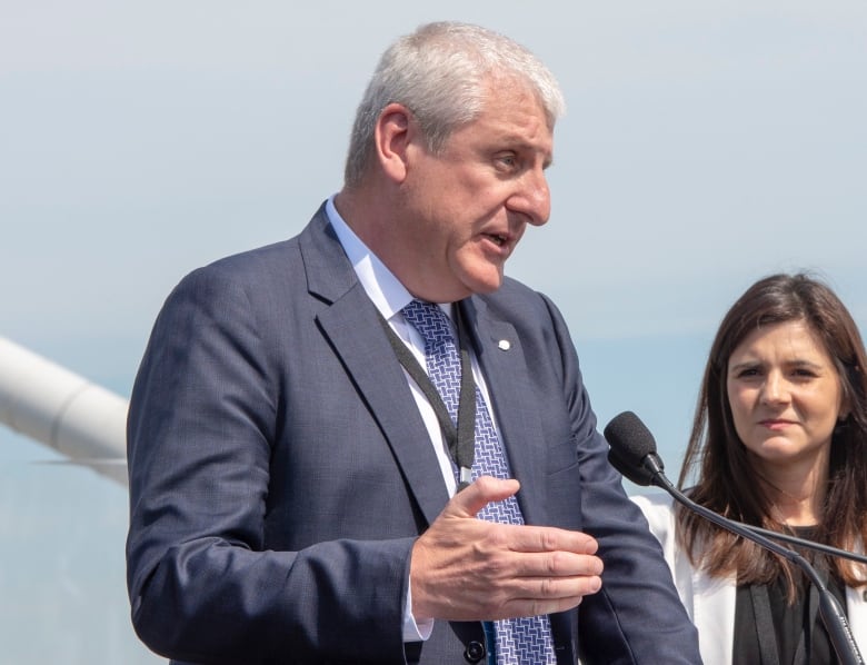 Man in a blue suit stands a mic outdoors.