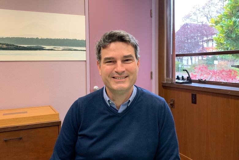 Kevin Murdoch smiles in an office with pink walls. He is wearing a blue sweater.