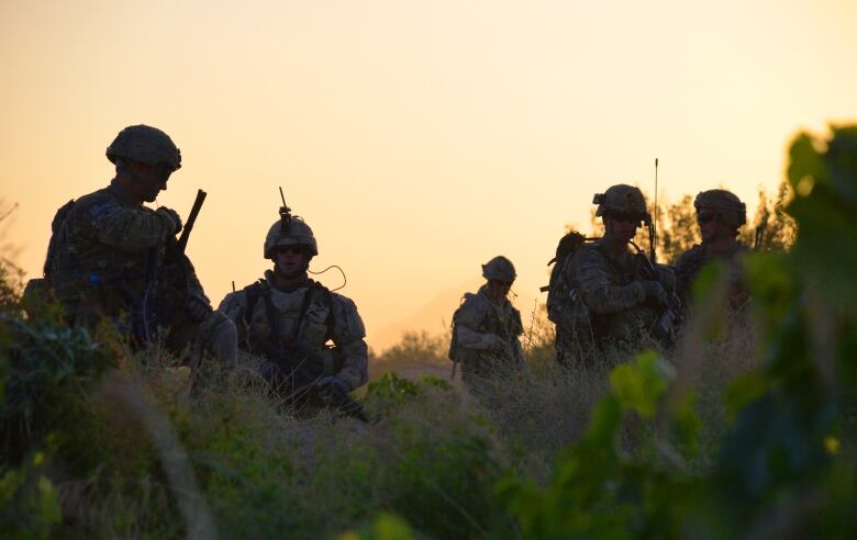 Soldiers stand silhouetted in front of the setting sun.