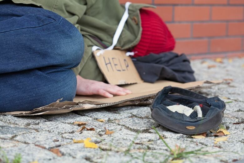 An unhoused person lies on the street asking for help.